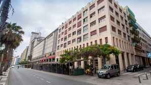 A multi-story hotel with a modern facade, a covered outdoor seating area, and a parking lot. - Apartment in Las Palmas Near Las Canteras Beach (Las Palmas de Gran Canaria)