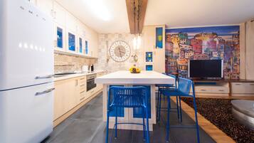 A modern kitchen with white cabinets, a central island with blue chairs, a large clock, and a colorful cityscape mural.