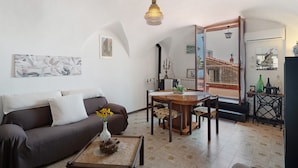 A living room with a sofa, coffee table, and a dining table with chairs. There is a chandelier, a radiator, and a mirror reflecting a staircase. - Holiday Home 'Basera' with Sea View, Wi-Fi & Air Conditioning (Cipressa)