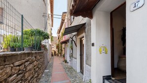 A narrow cobblestone alley with a stone wall on one side and a building entrance with a welcome mat. - Holiday Home 'Basera' with Sea View, Wi-Fi & Air Conditioning (Cipressa)
