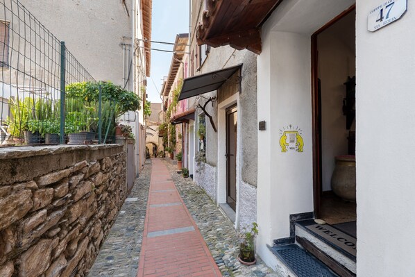 A narrow cobblestone alley with a stone wall on one side and a building entrance with a welcome mat.