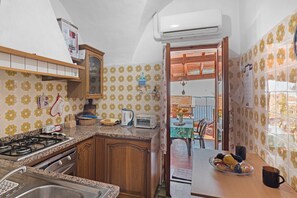 A kitchen with a gas stove, oven, and sink. There is a wooden cabinet and a countertop with a kettle and toaster.