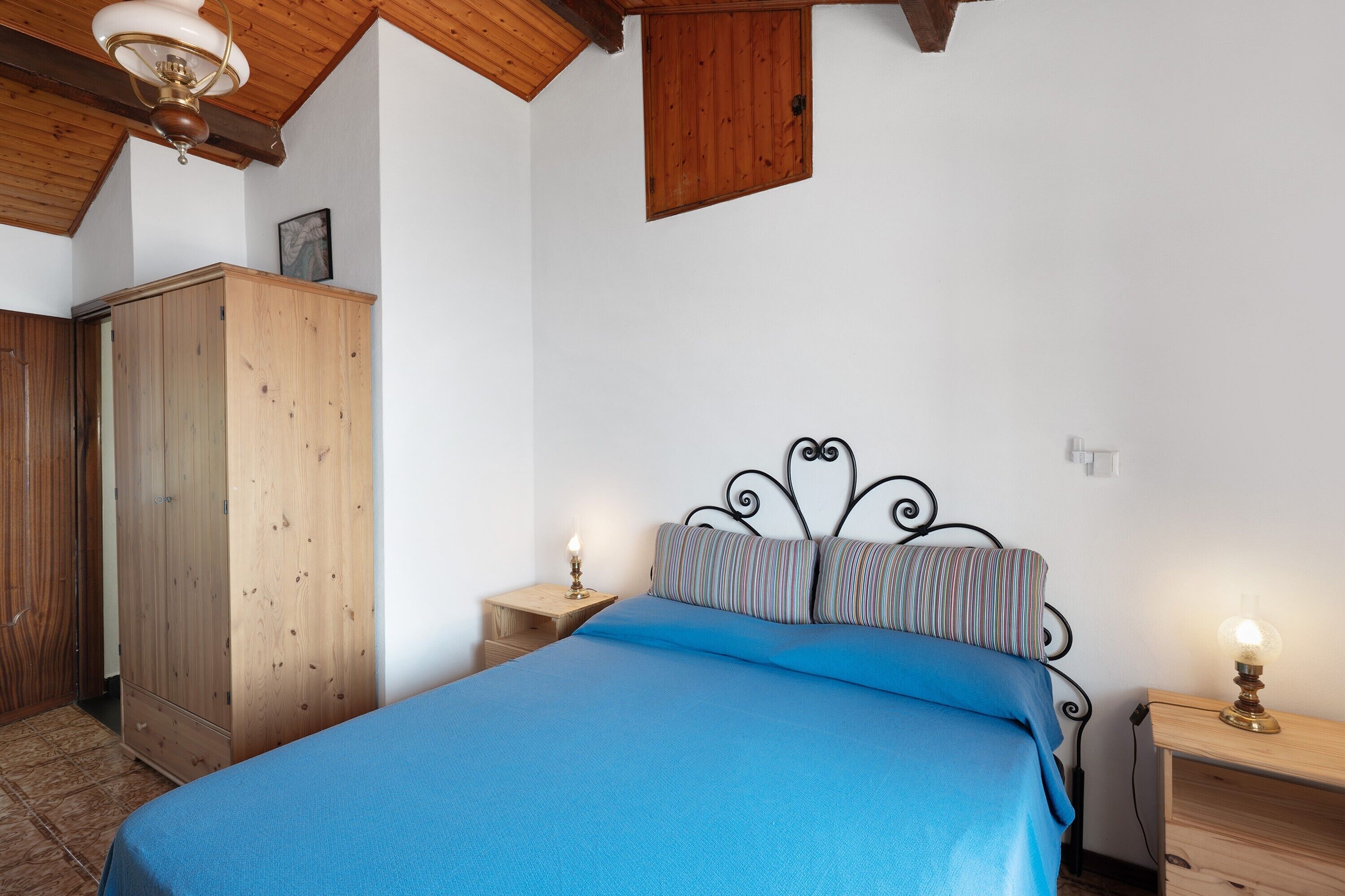 Ein Schlafzimmer mit Bett, Holzschrank, Nachttisch mit Lampe und Deckenventilator.