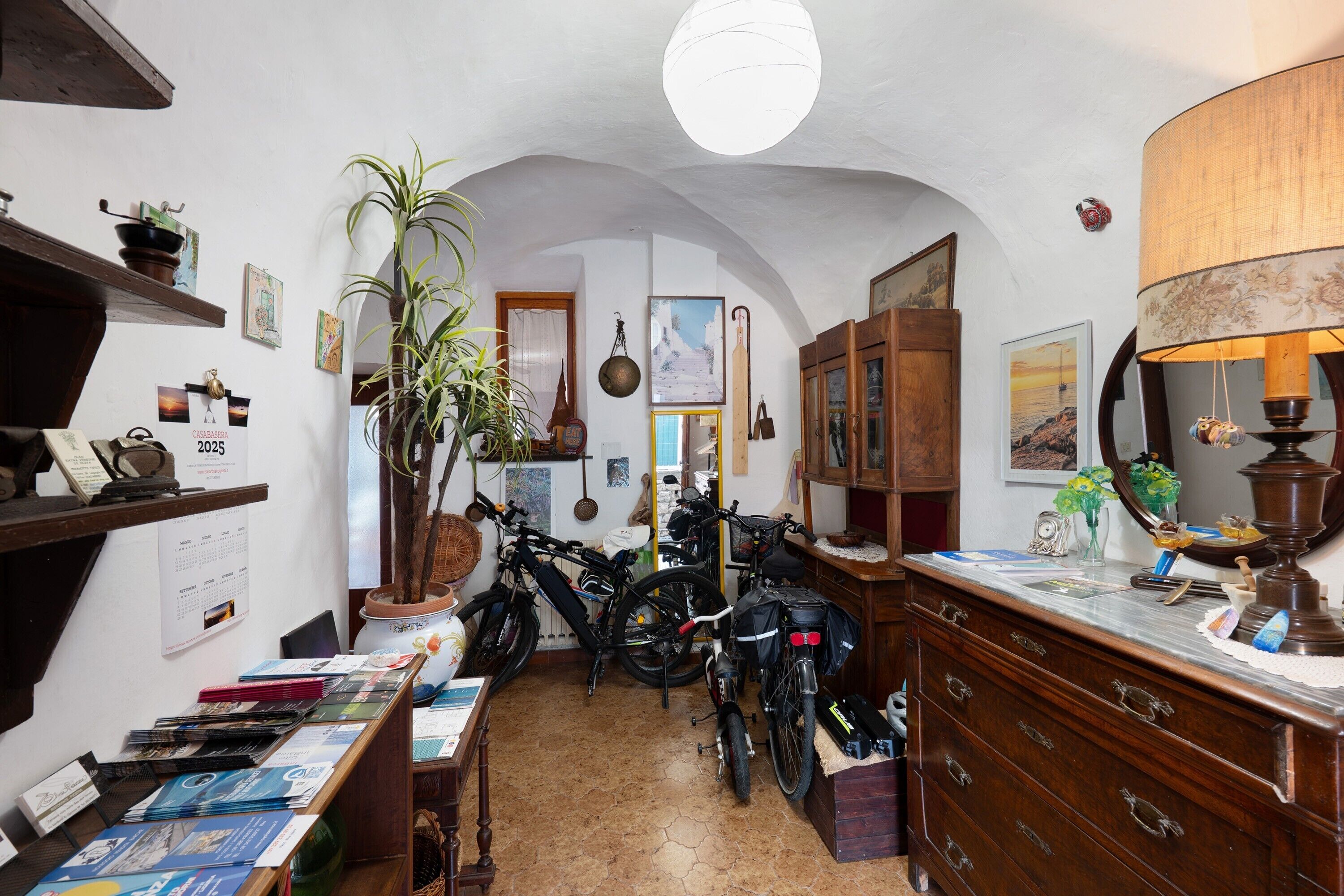 A room with a wooden dresser, a bicycle, a potted plant, and a calendar on the wall.