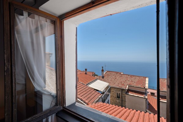 A window with a view of terracotta rooftops and the sea.