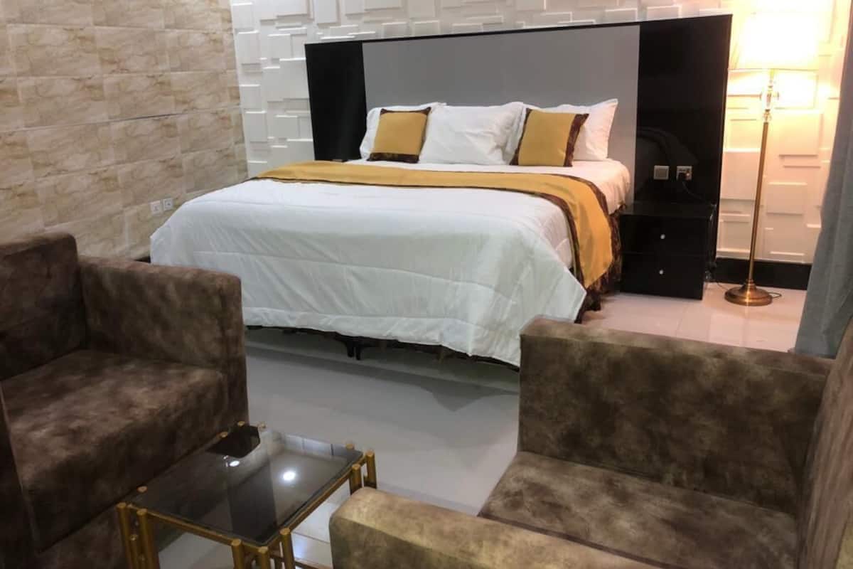 A hotel room with a large bed, two armchairs, a small table, and a modern wall design.