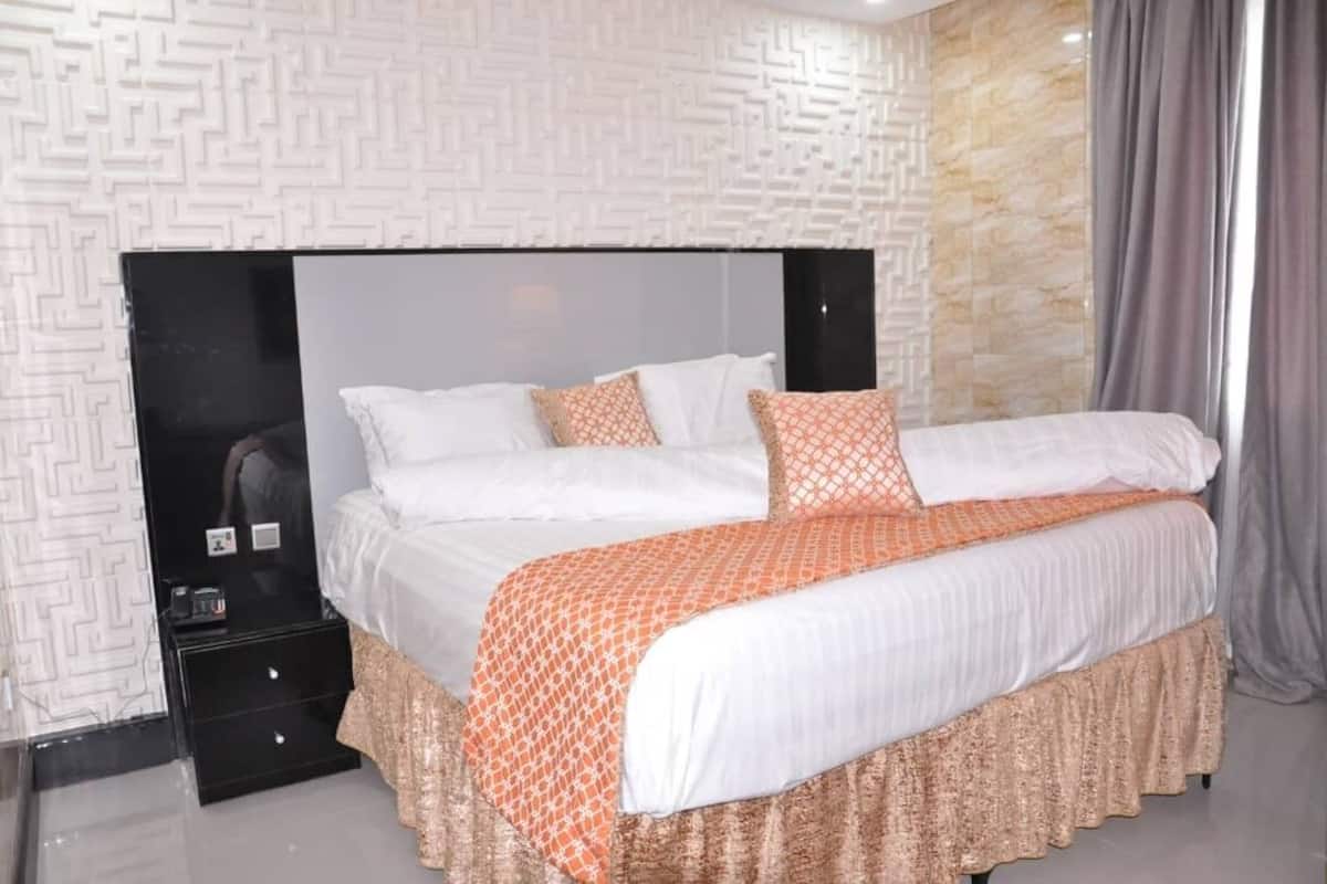A modern bedroom with a large bed, a black headboard, and a patterned wall.