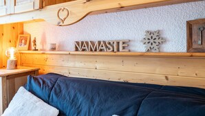 A wooden cabin interior with a bed, a shelf with decorative items, and the word 'NAMASTE' on the wall.