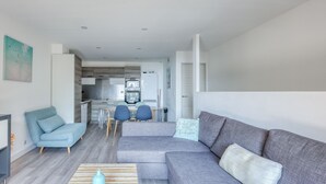 A modern living room with a grey sectional sofa, a blue armchair, and a dining area with a small table and chairs.