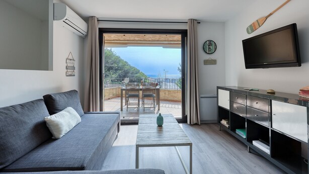 A modern living room with a sofa, a coffee table, a TV, and a balcony with a view.