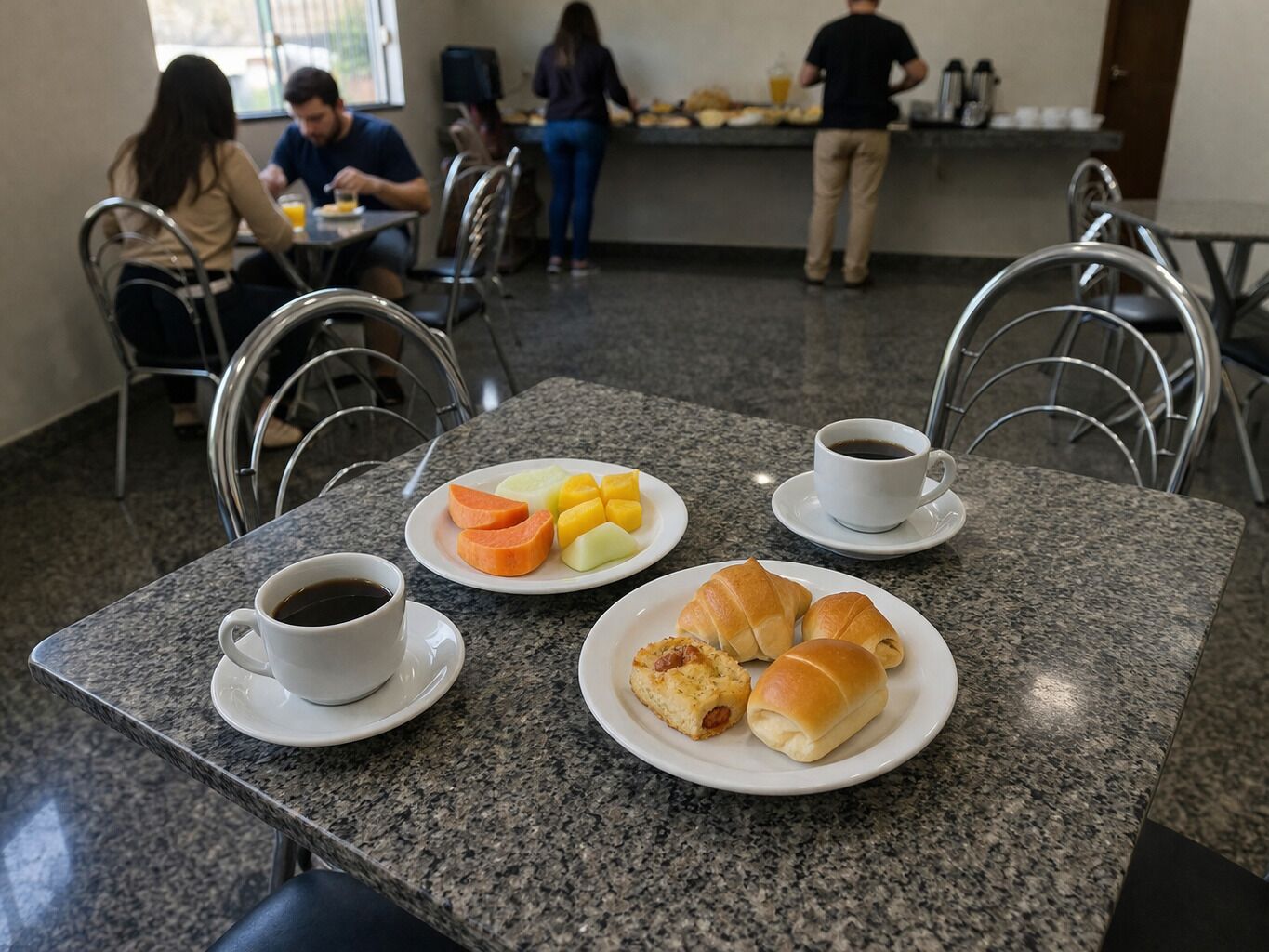 A dining area with granite tables, chairs, plates of food, and cups of coffee.
