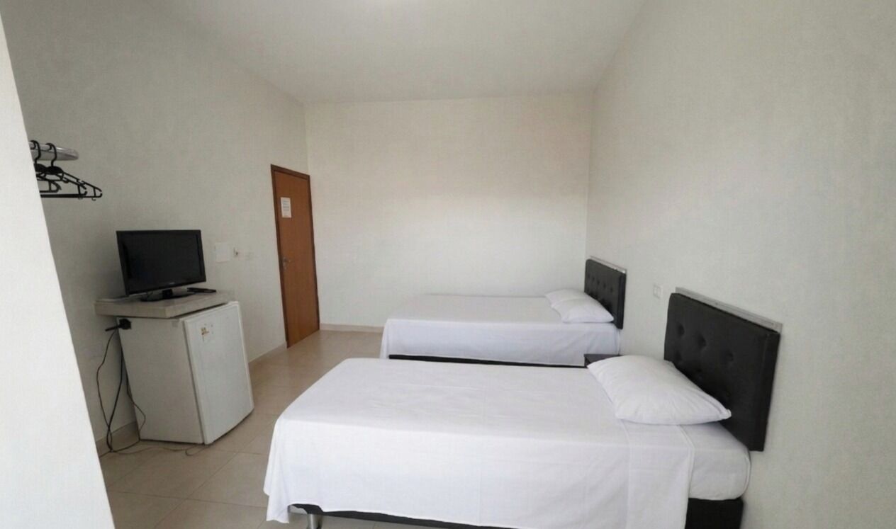 A small, clean room with two beds, a television, and a refrigerator.