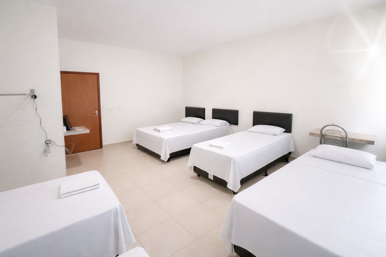 Habitación de hotel con dos camas individuales, una puerta de madera y una mesita con una silla.