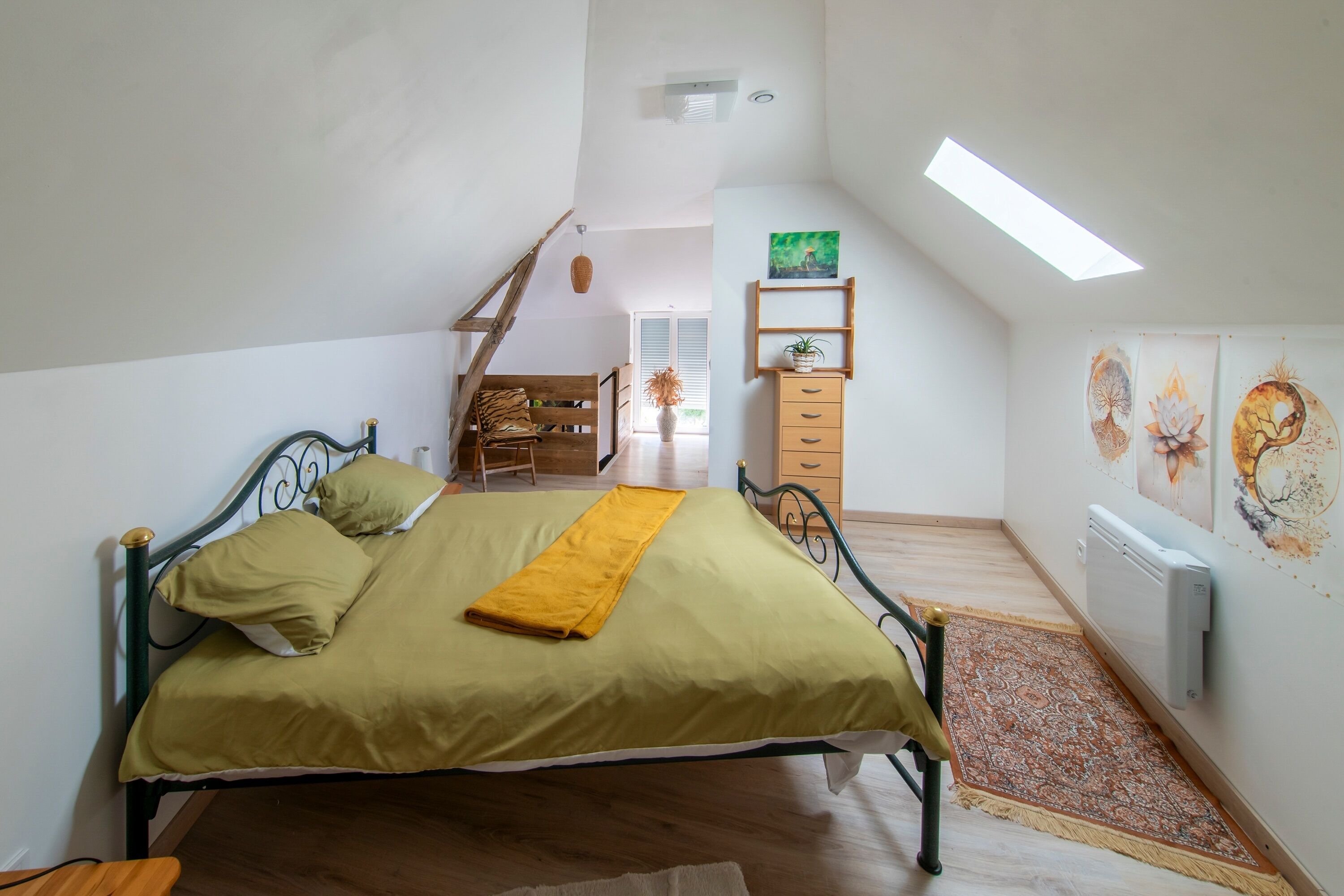 A bedroom with a bed, a wooden chair, a small table, a radiator, and a window.