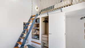 Ein Schlafzimmer mit einem Bett, einer blauen Matratze, einer Holzleiter, einem Schrank mit Regalen und einer Tür.