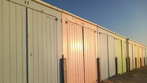 Une rangée de cabanes de plage numérotées, dont le sol est recouvert de sable.