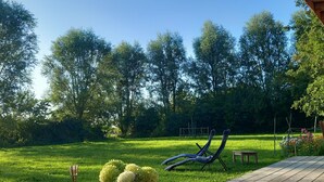 Une terrasse en bois avec une table de pique-nique, une sculpture en métal et un pot de fleurs contenant des fleurs jaunes.