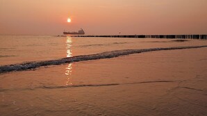 Une plage au coucher du soleil, avec une jetée qui s’avance dans l’eau.