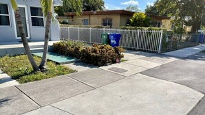 A residential street with a sidewalk, a white fence, and two blue recycling bins.