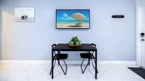 A dining area with a table, two chairs, a potted plant, and a beach-themed painting.
