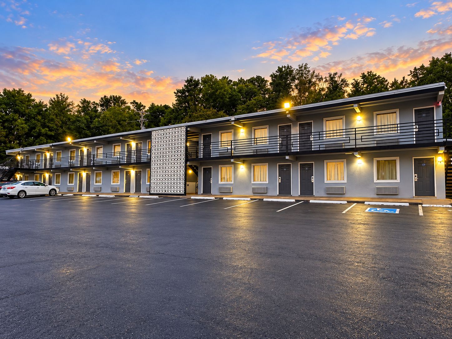A motel with a two-story structure, multiple rooms, a parking lot, and a decorative wall.