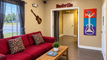 Un hall de hotel con un sofá rojo, una mesa de centro de madera con revistas, una obra de arte de una guitarra y una pintura de una guitarra.