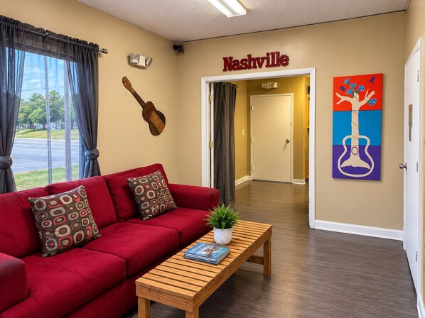 A hotel lobby with a red sofa, a wooden coffee table with magazines, a guitar wall art, and a guitar painting. - expressway inn (Nashville)