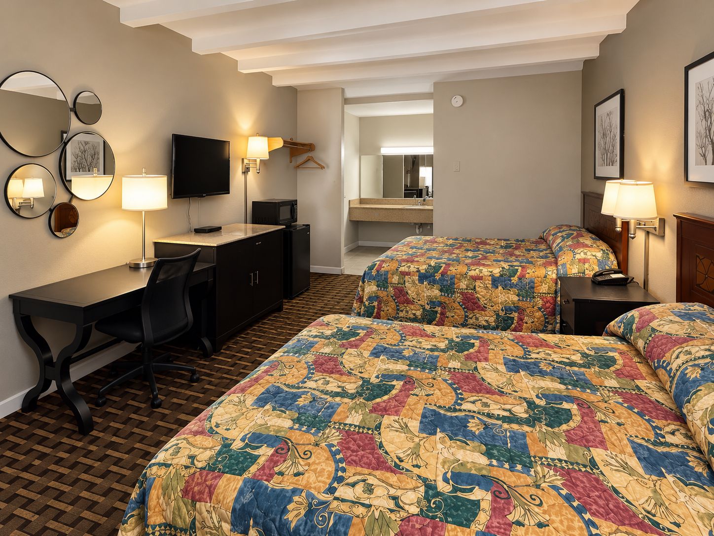 Ett hotellrum med två sängar, ett skrivbord, en stol, en TV, en spegel och en mikrovågsugn.