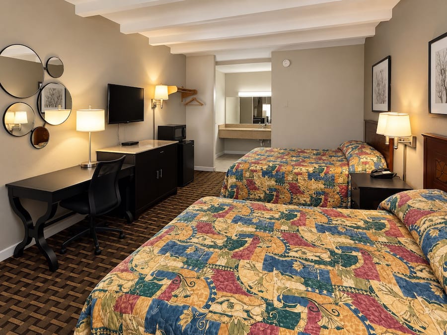 A hotel room with two beds, a desk, a chair, a TV, a mirror, and a microwave.