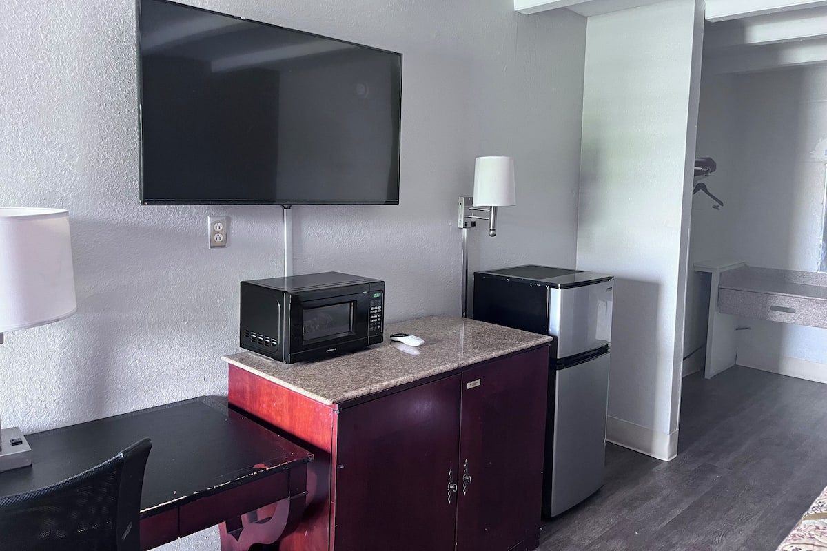 A compact kitchenette with a microwave, refrigerator, and a flat-screen TV mounted on the wall.