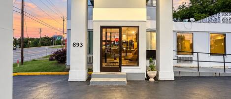 A building with a numbered address sign, a glass door entrance, and a paved area in front.