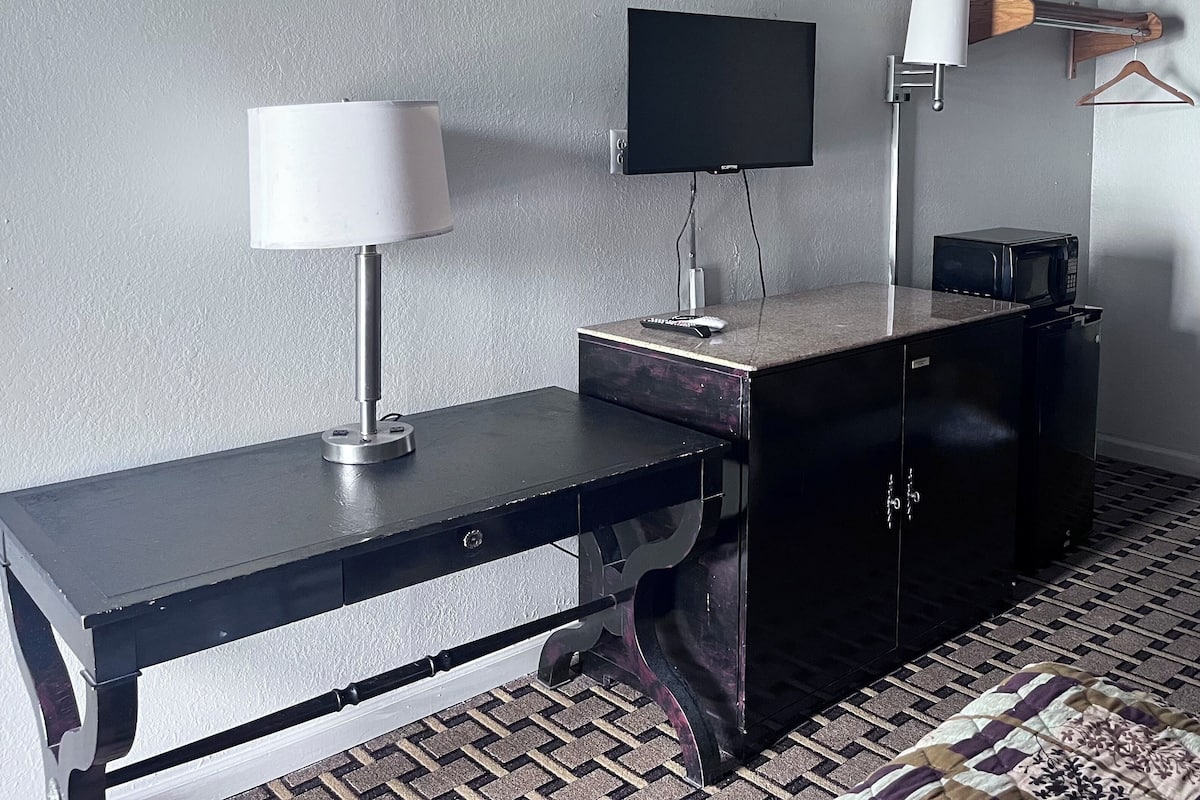 A modern room with a black desk, a mounted TV, a lamp, and a wooden hanger on the wall.
