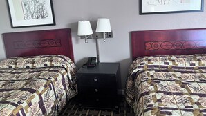 Habitación de hotel con dos camas, cada una con un edredón estampado, una mesita de noche con lámpara y dos cuadros enmarcados en la pared.