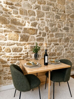 A dining table set with plates, glasses, a bottle, and candles against a stone wall. - 1599 Perche (Paris)