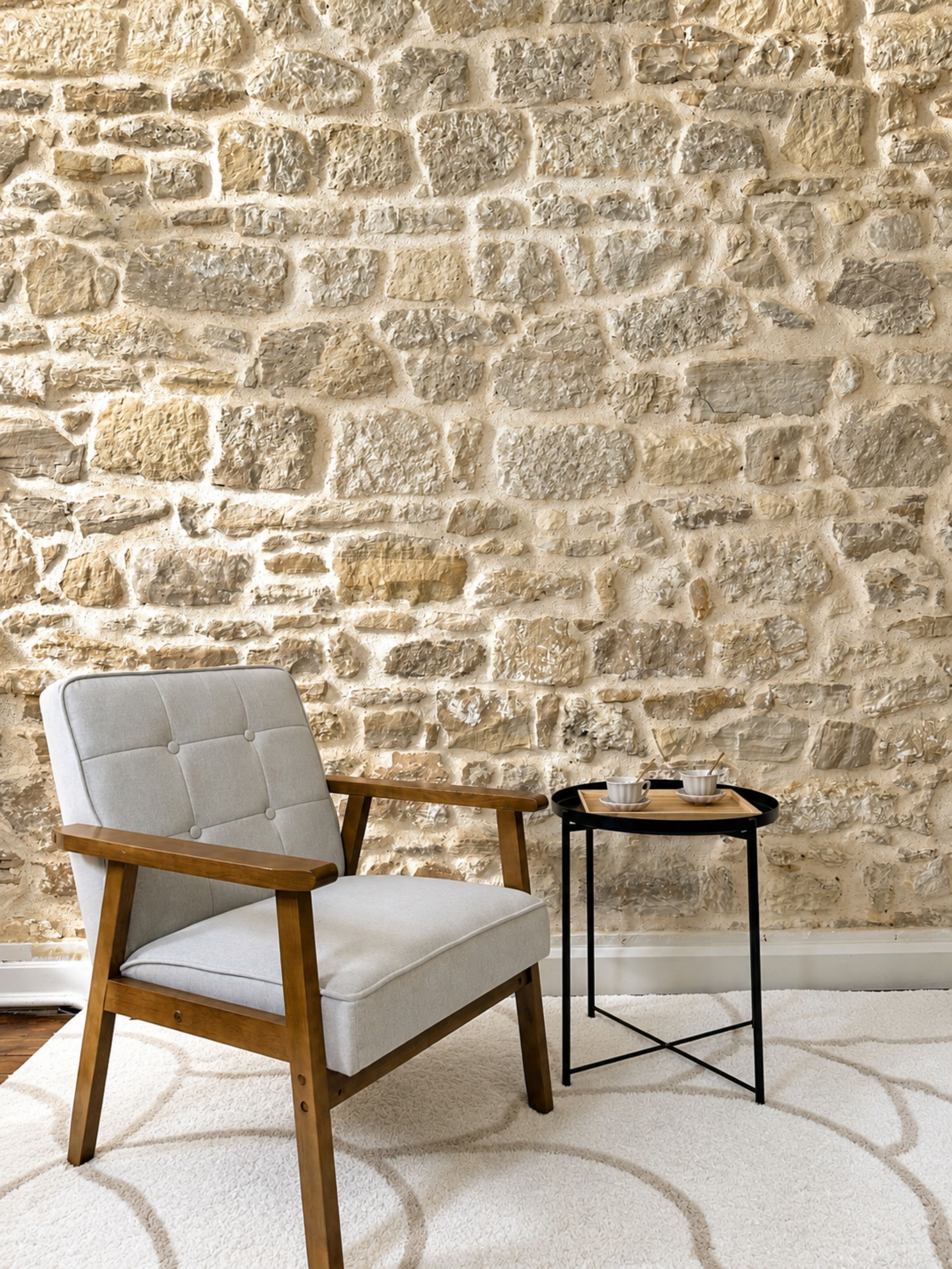 A room with a stone wall, a cushioned chair, a small table with a tray, and a white carpet.