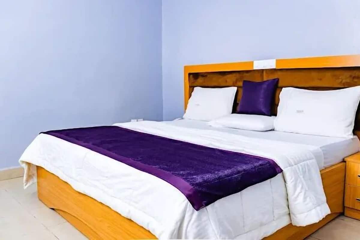A neatly made bed with a wooden headboard, white bedding, and a purple throw blanket.