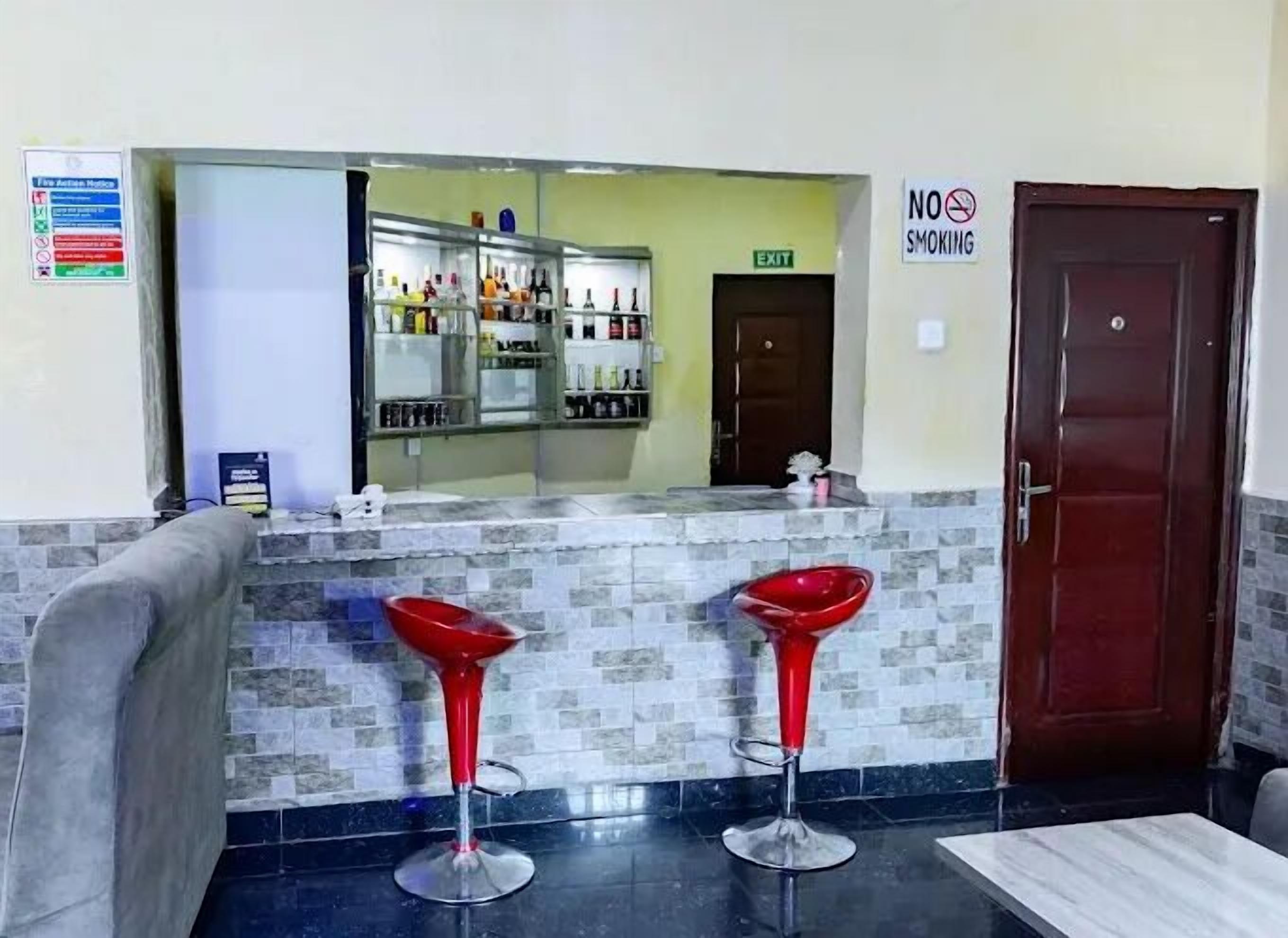 Un área de recepción con mostrador, dos taburetes rojos, un espejo, un letrero de 'No Fumar' y una puerta.