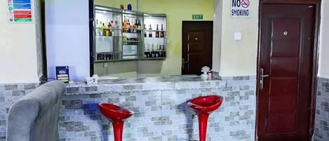 Un área de recepción con mostrador, dos taburetes rojos, un espejo, un letrero de 'No Fumar' y una puerta.