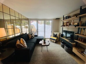 En moderne stue med en sort sofa, et sofabord og et fjernsyn på et træstel.