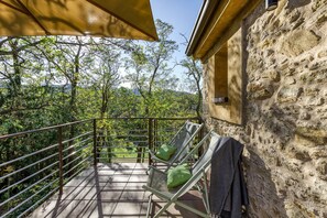 Un balcone con parete in pietra, ringhiera in metallo e vista su alberi e colline.