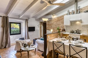 Un coin repas chaleureux avec une table dressée pour quatre personnes, une cuisine équipée d’appareils modernes et un mur en briques.