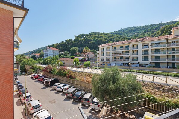 Un immeuble à plusieurs étages doté de balcons, un parking rempli de voitures et, au loin, un paysage vallonné.
