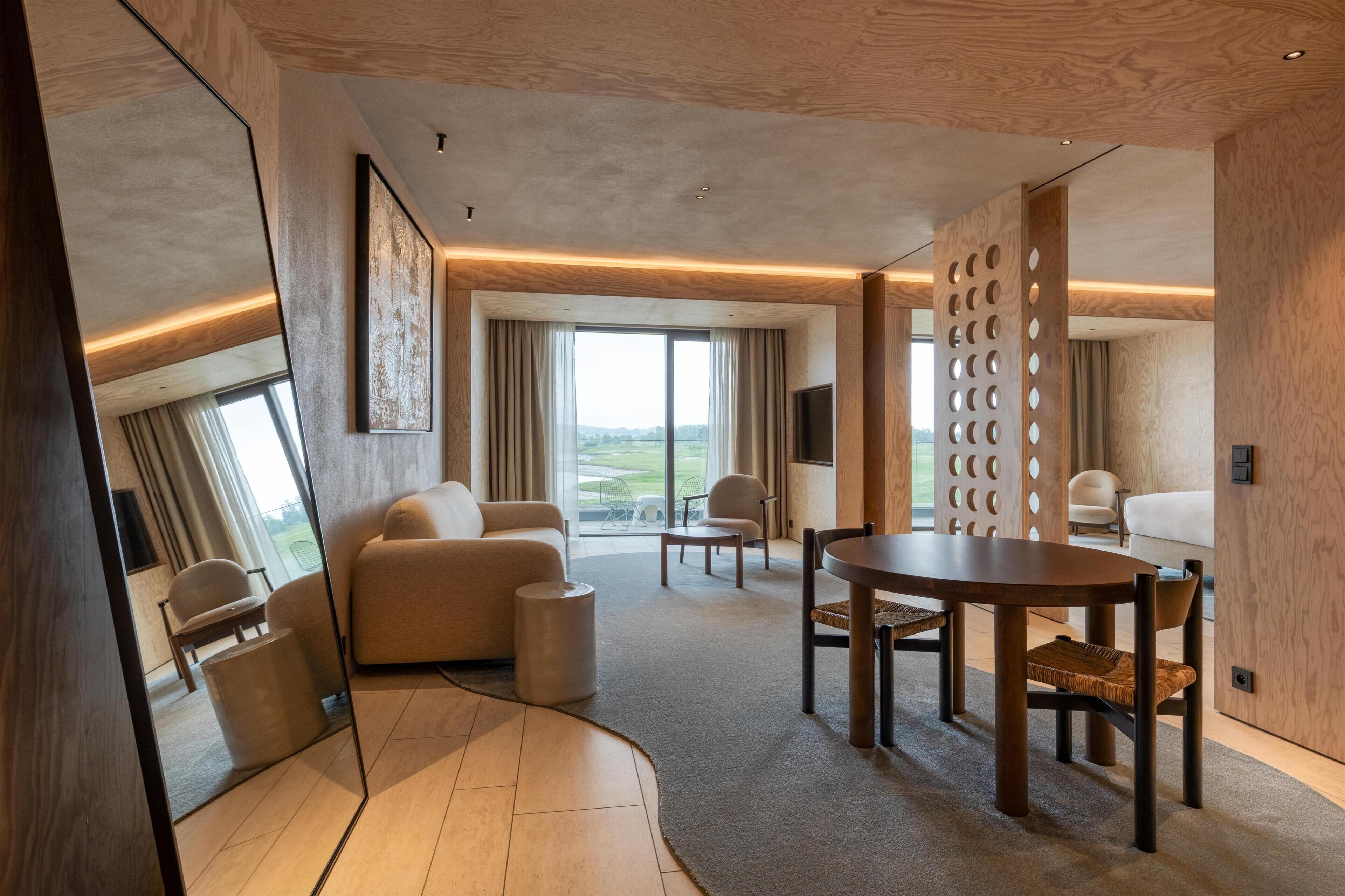 A modern hotel room with a large window, a dining area, and a seating area.