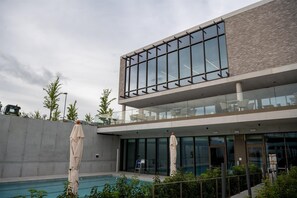 A modern building with a pool area, featuring a glass facade and outdoor seating.