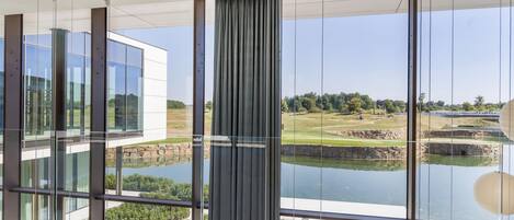 Un interior moderno con ventanas amplias que ofrecen vistas a un jardín ajardinado con un estanque y edificios a lo lejos.