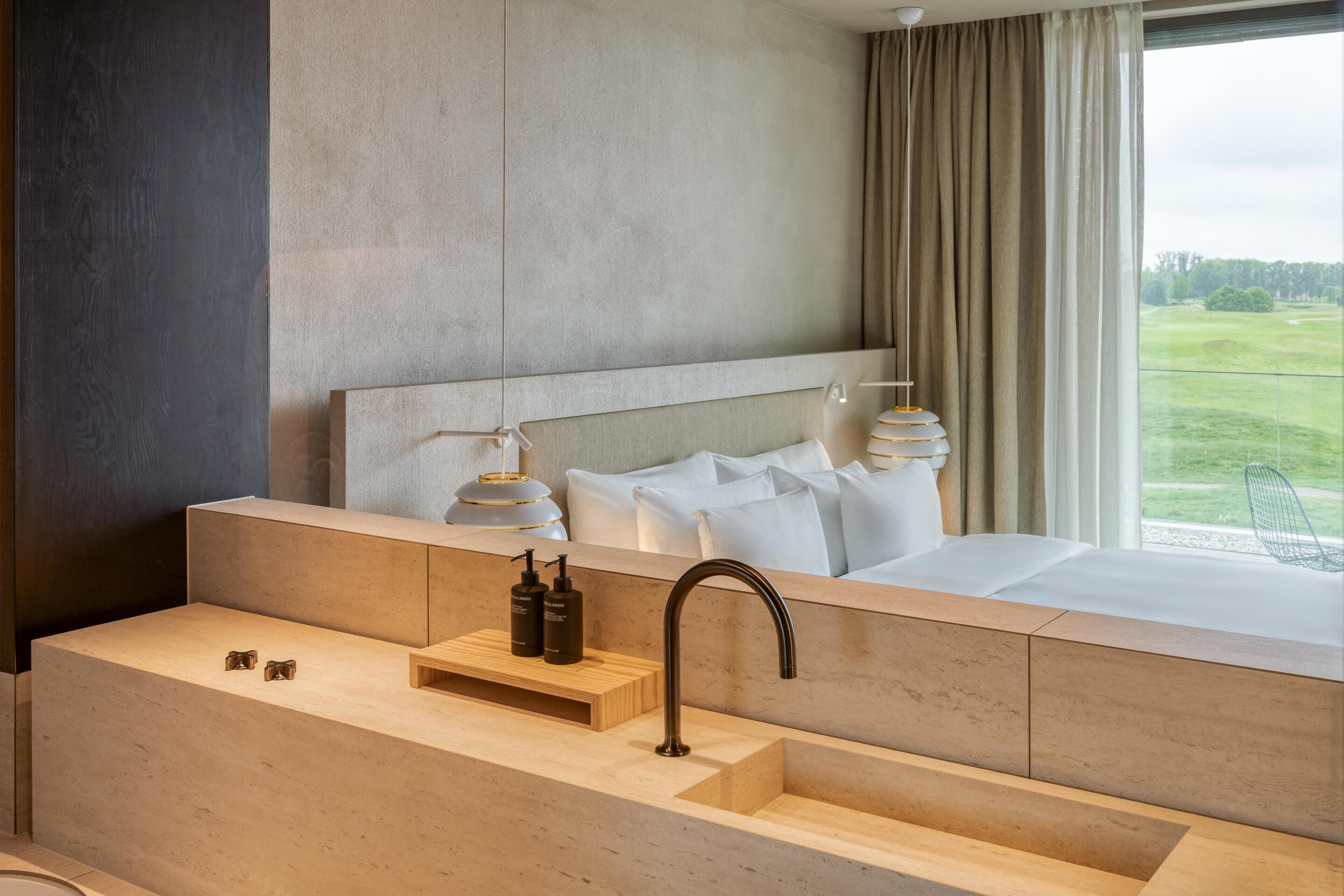 Une chambre d’hôtel moderne avec un grand lit, une coiffeuse en bois avec un lavabo et une vue sur un terrain de golf.