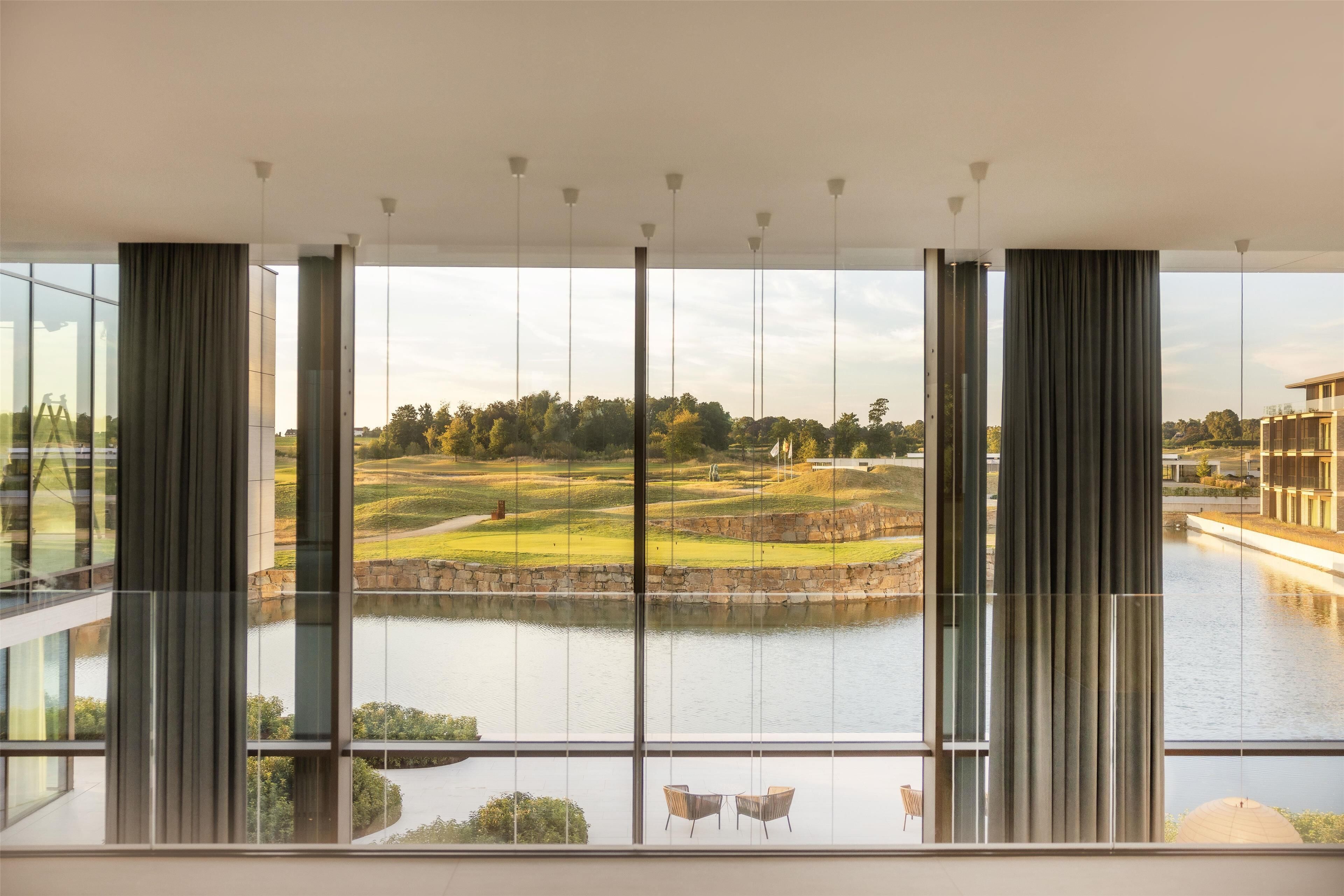 A modern room with large windows offering a view of a golf course and a lake.