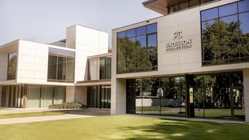 A modern building with a glass facade, a sign reading 'RADISSON COLLECTION', and a well-maintained lawn in front.