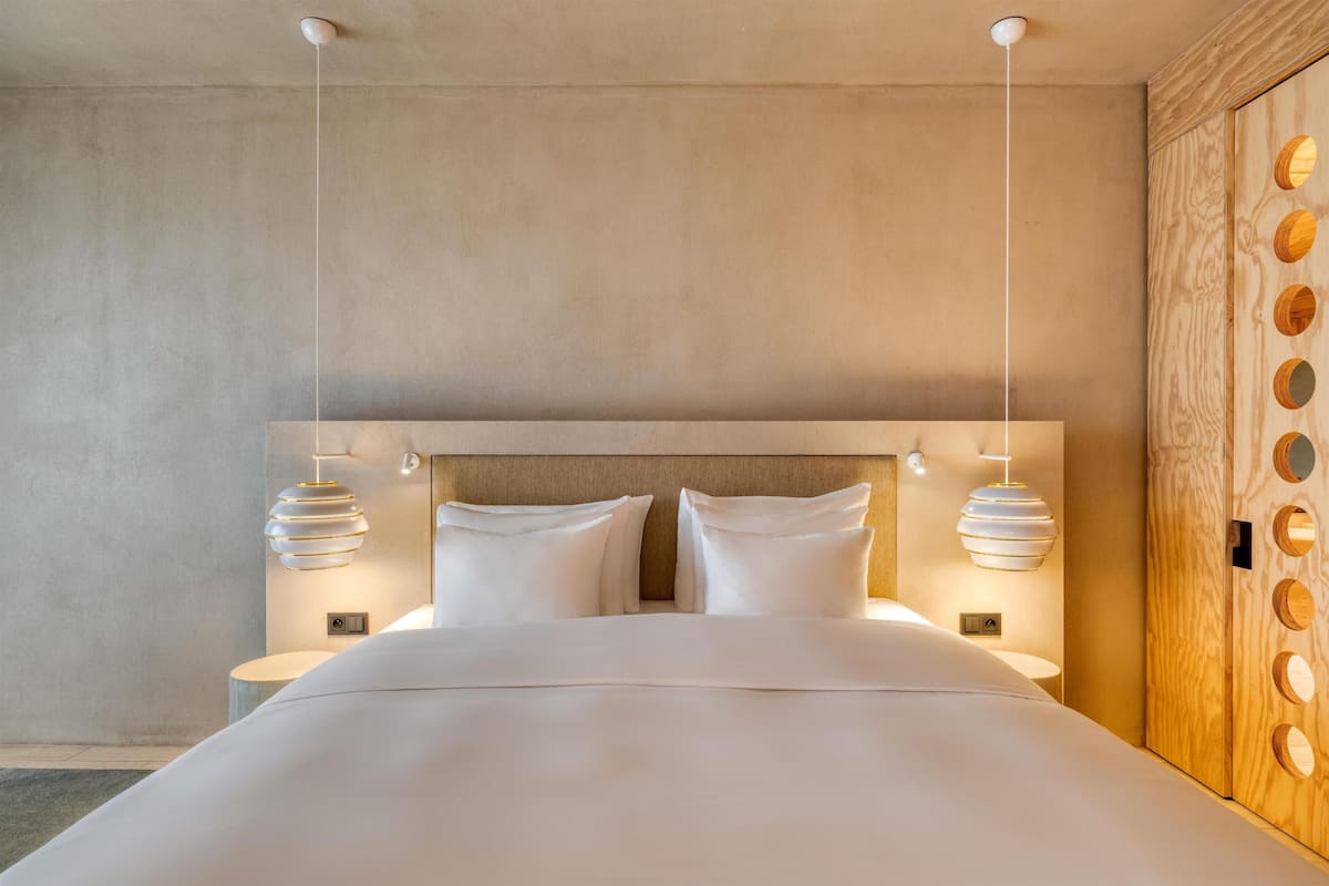 Ett modernt hotellrum med en stor säng, två sängbord och en garderob i trä med cirkelformade utskärningar.