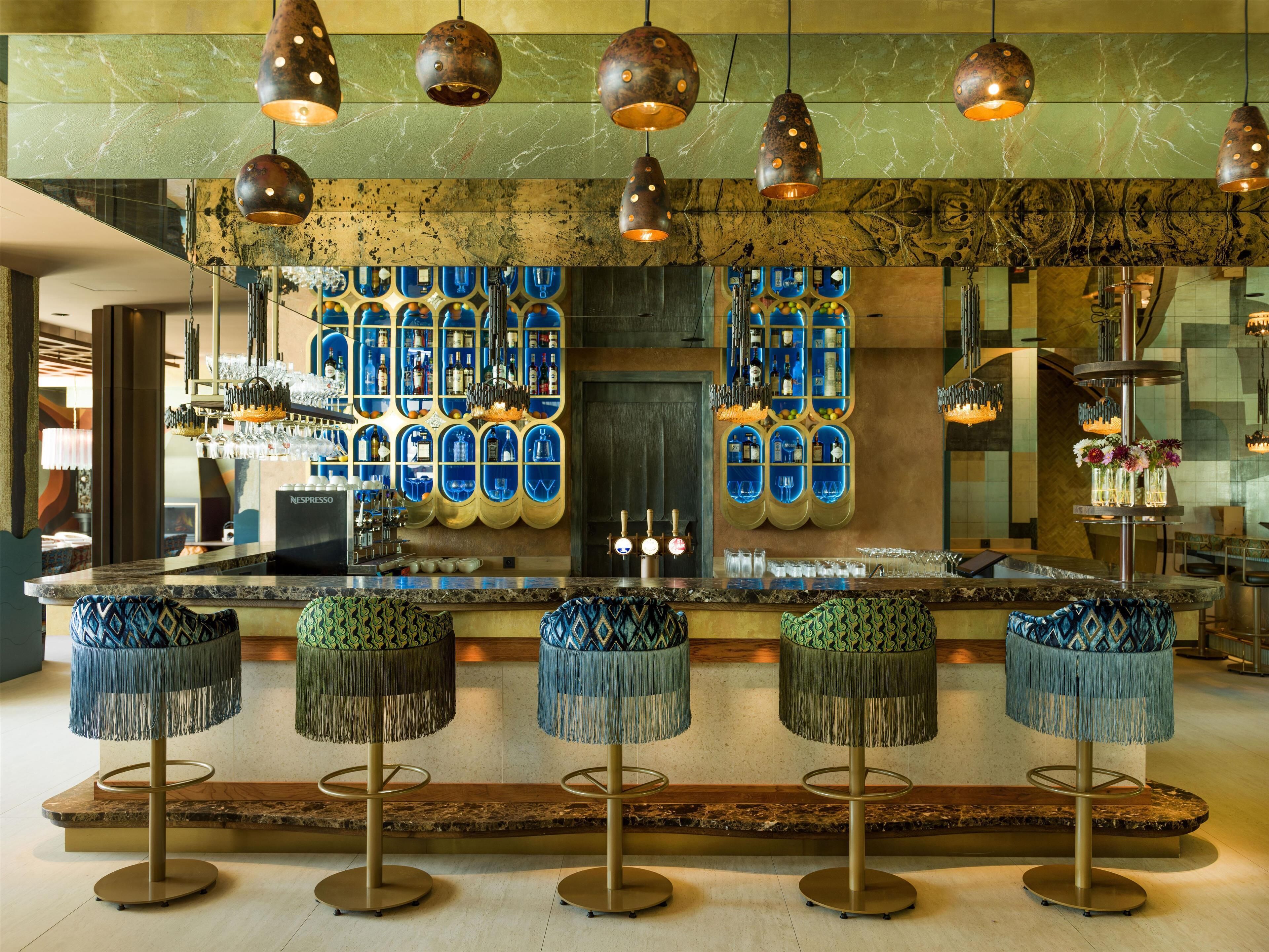 A bar area with a marble countertop, blue bar stools, and hanging pendant lights.